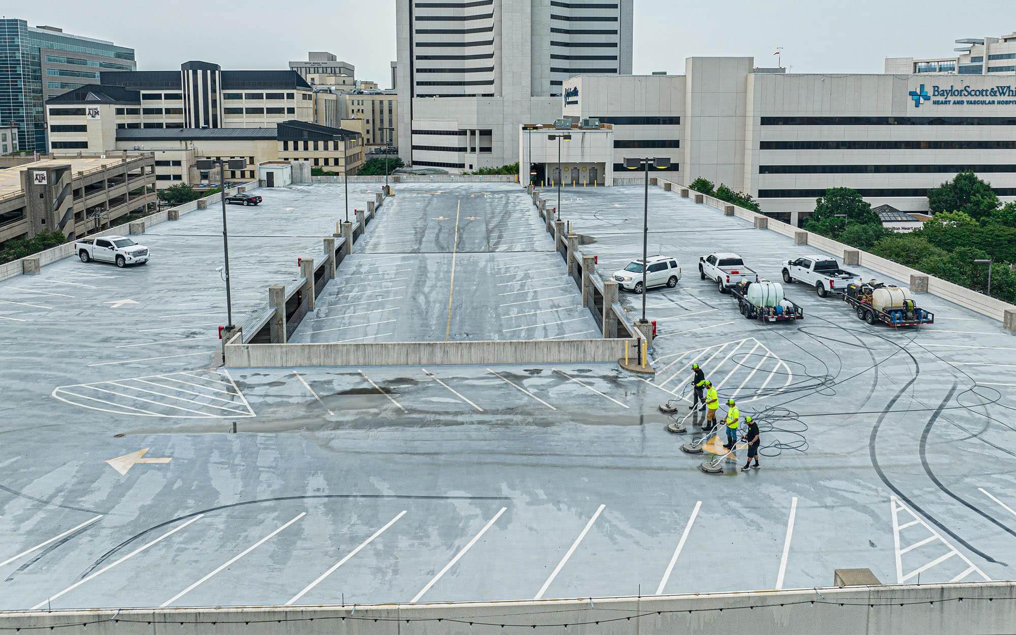 Aerial side view of four men cleaning a top level parking lot