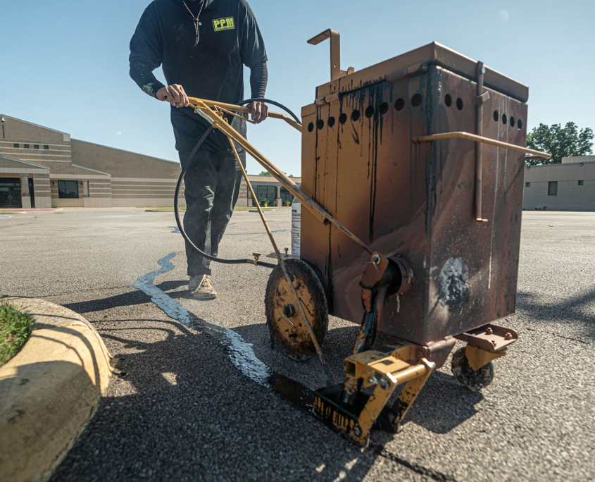 Close up of man pushing machine that fills in parking lot cracks