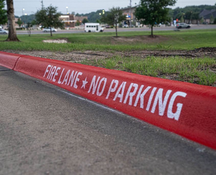 Side view of a fire lane curb with white text that reads Fire Lane No Parking