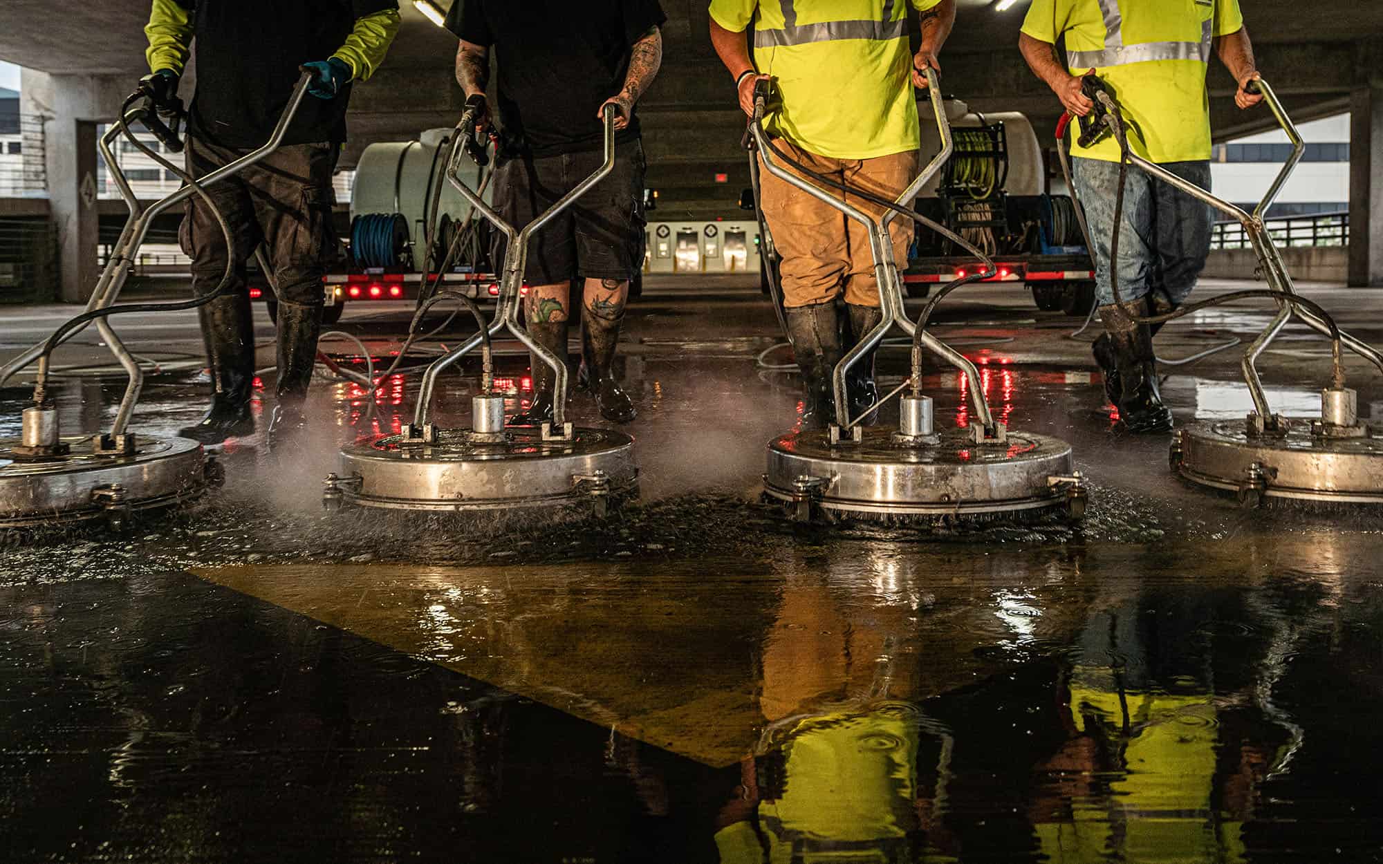 Worm's eye view of four men operating heavy duty cleaning machines reflected in water
