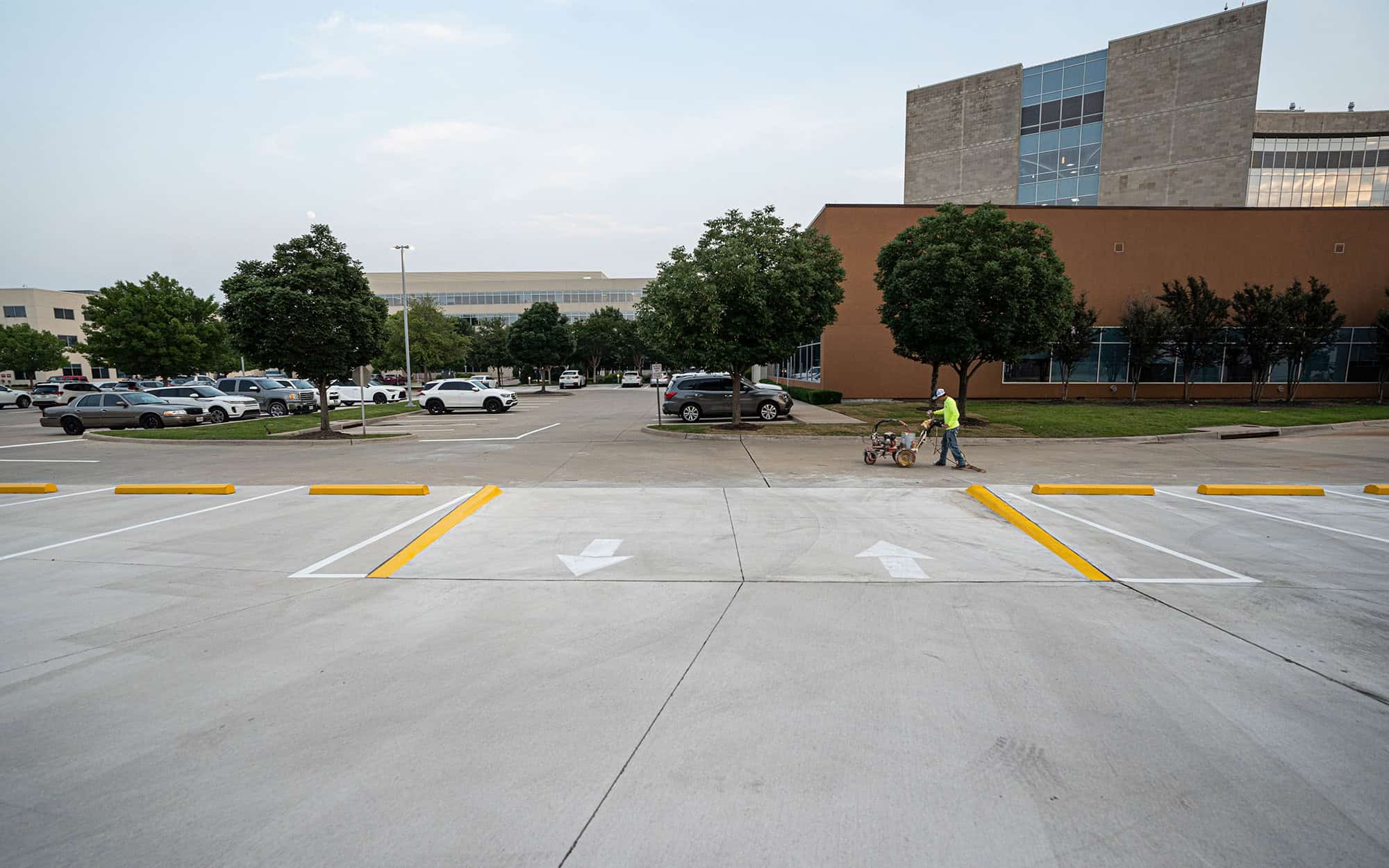 wide panoramic view of a man pushing parking lot painting equipment in parking lot of a medical facility