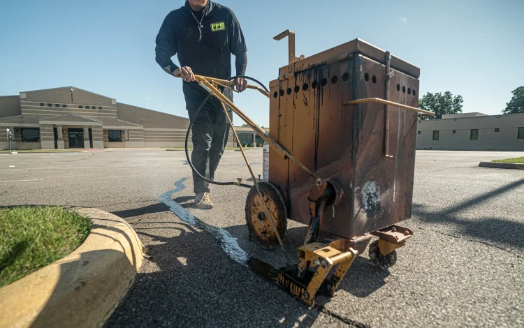 A person uses a machine to fill cracks in an empty parking lot