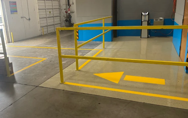 Industrial area with smooth concrete floor, yellow lines, arrows, and metal railing