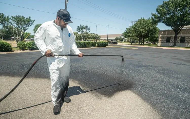Man in white protective suit spraying black sealant on a parking lot