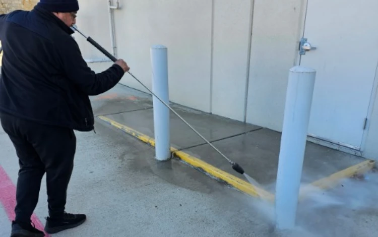 A person uses a pressure washer to clean a concrete sidewalk A person uses a pressure washer to clean a concrete sidewalk