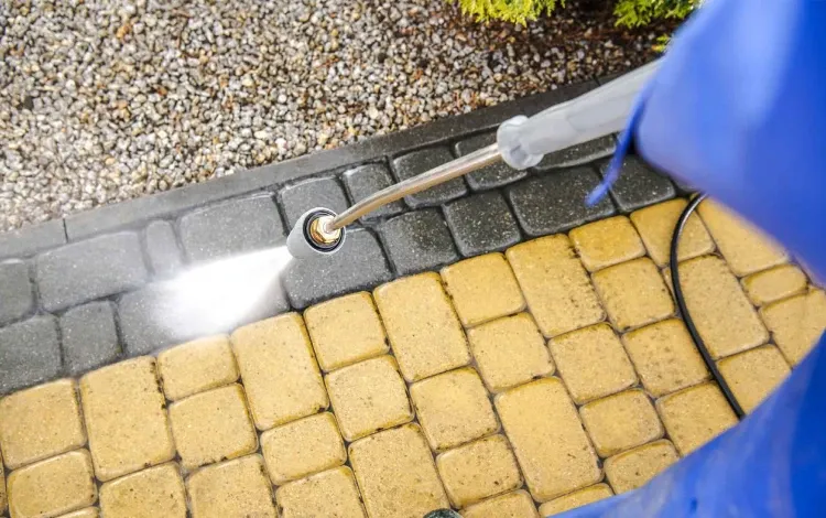 A power washer cleaning a patio of yellow and dark gray pavers