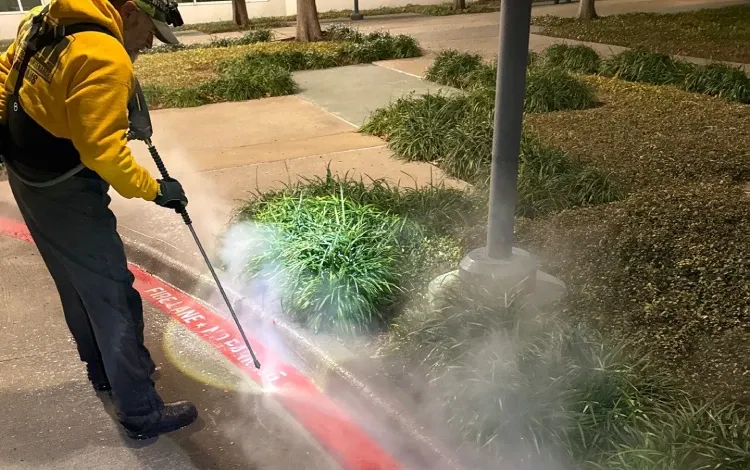 A PPM technician pressure washes a red curb marked FIRE LANE A PPM technician pressure washes a red curb marked FIRE LANE